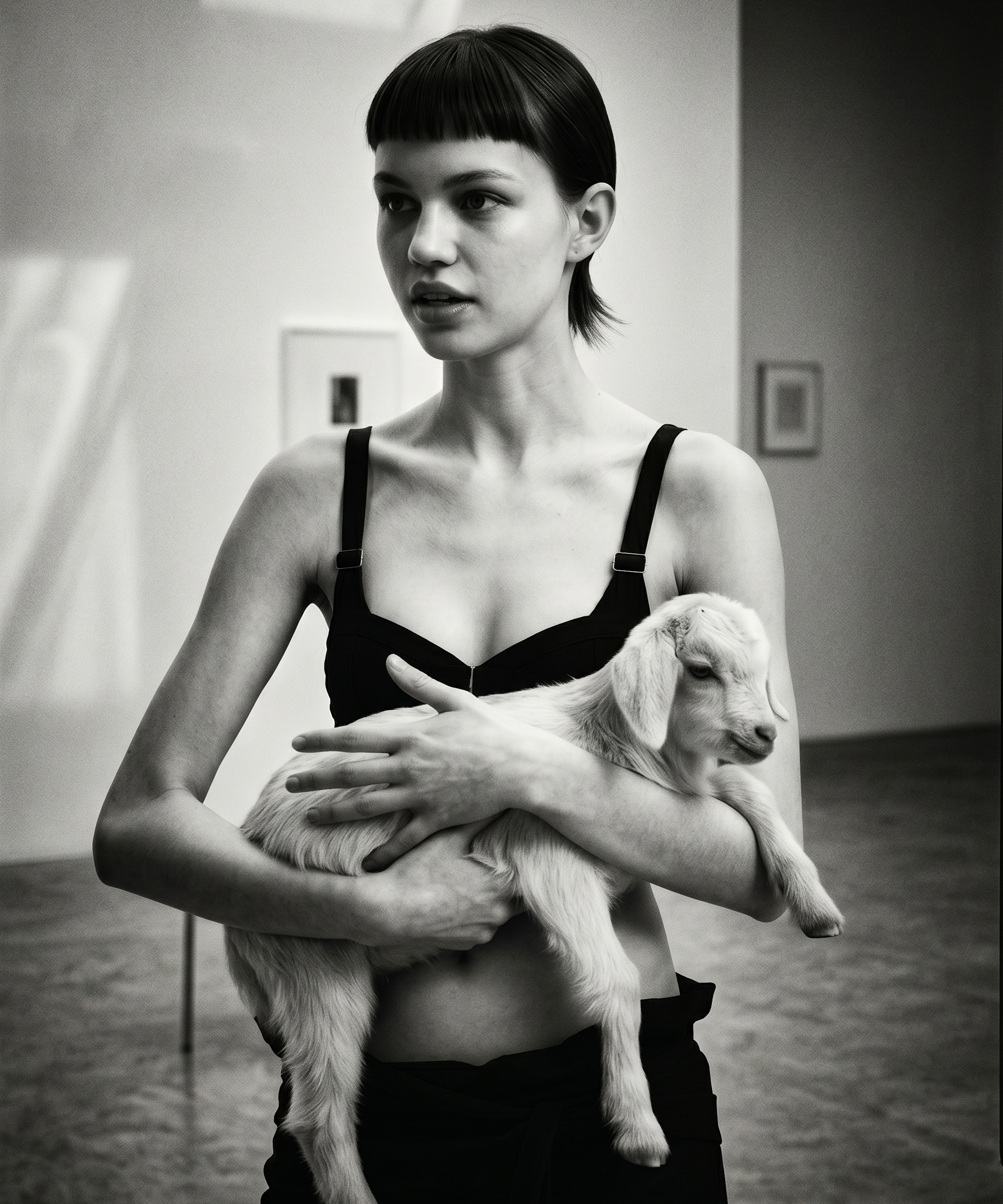 Intelligence Matters — chapter two: a gallery portrait, a model in black cradling a small white goat, framed works on the wall behind