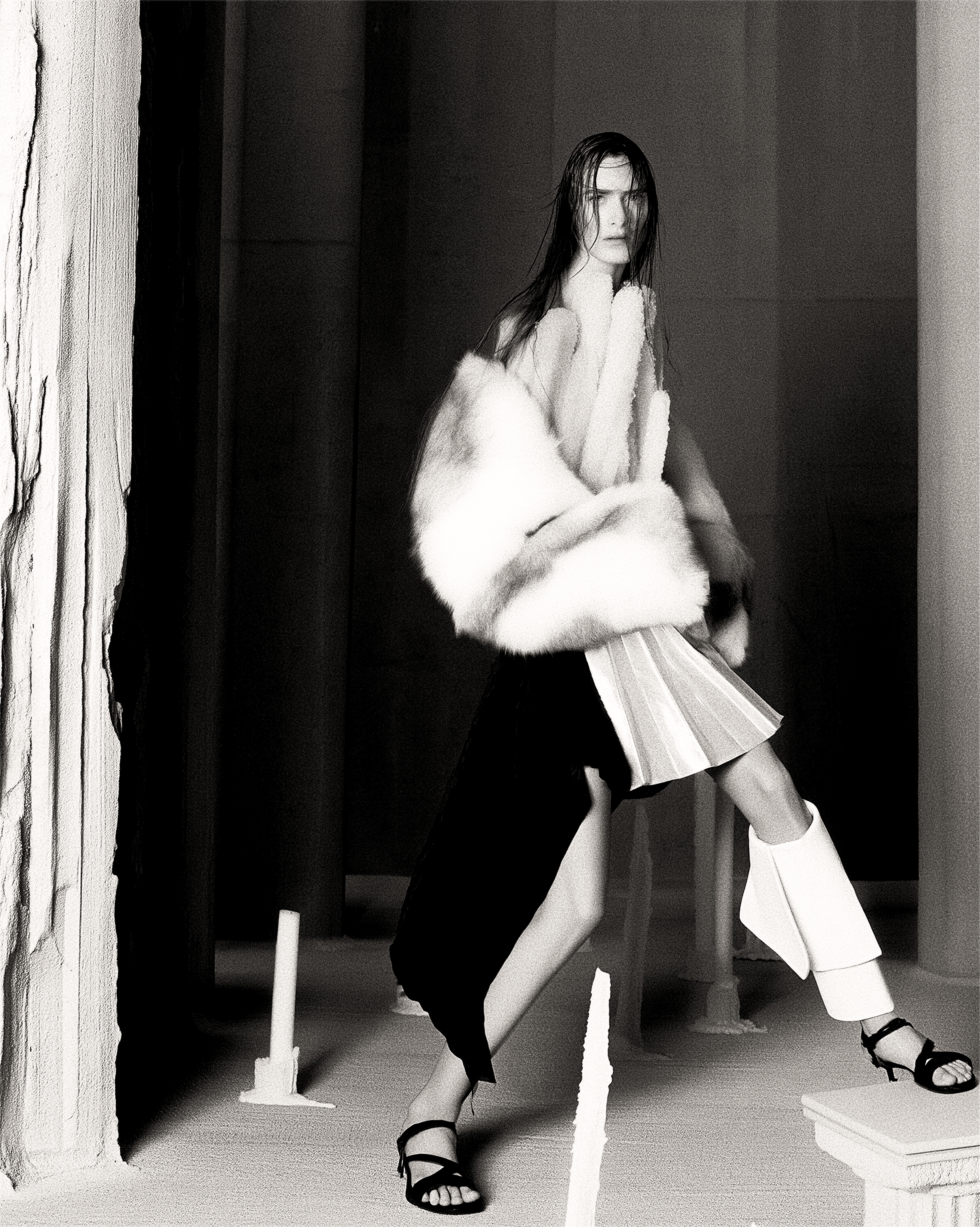 Full-length in fur and draped white, in motion between columns