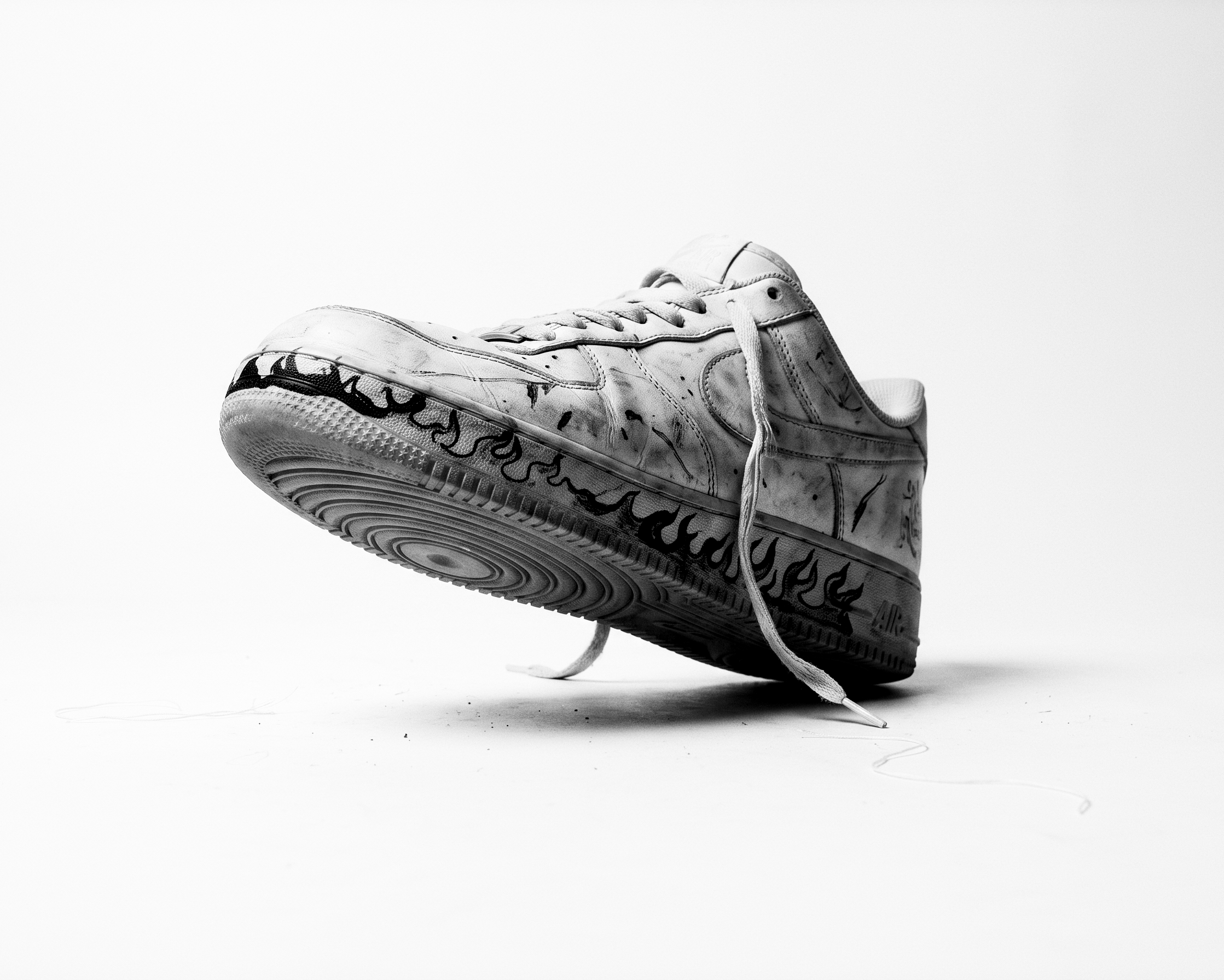 A white sneaker with black flame markings, tilted above a white background.