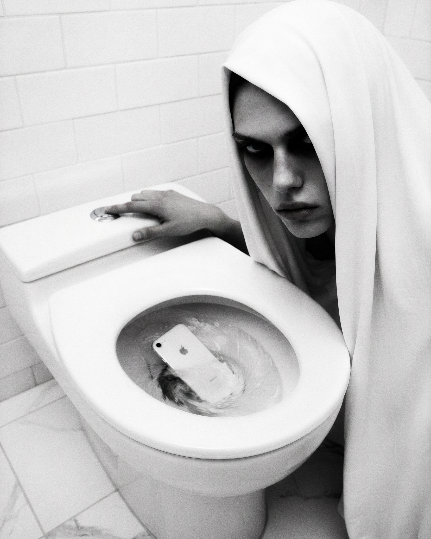 A hooded figure crouched over a white toilet, glaring at the camera, a smartphone submerged mid-flush in the bowl.