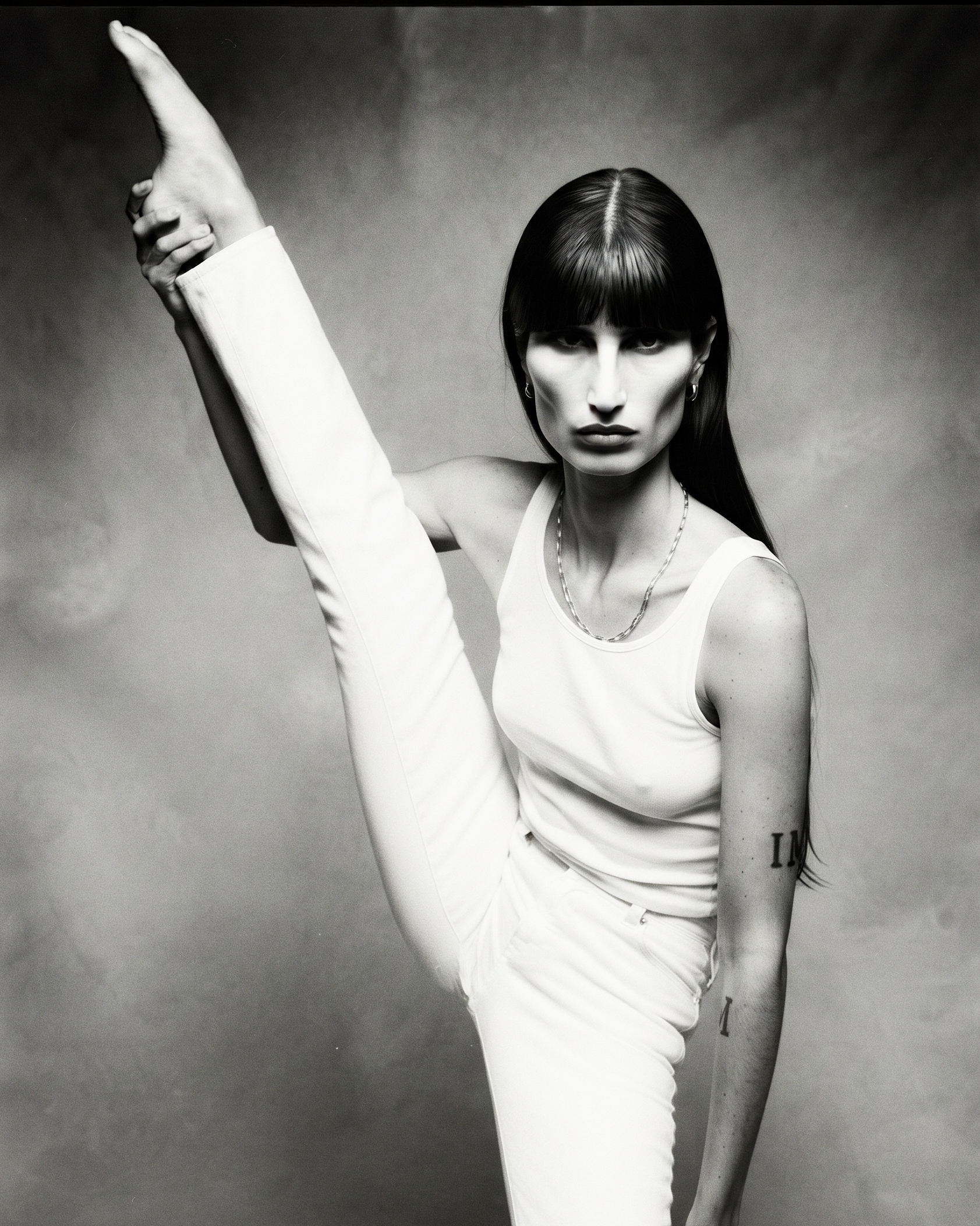 Recent — a monochrome full-body figure in a white tank and jeans holds one foot vertically above her head; IM is marked on her forearm