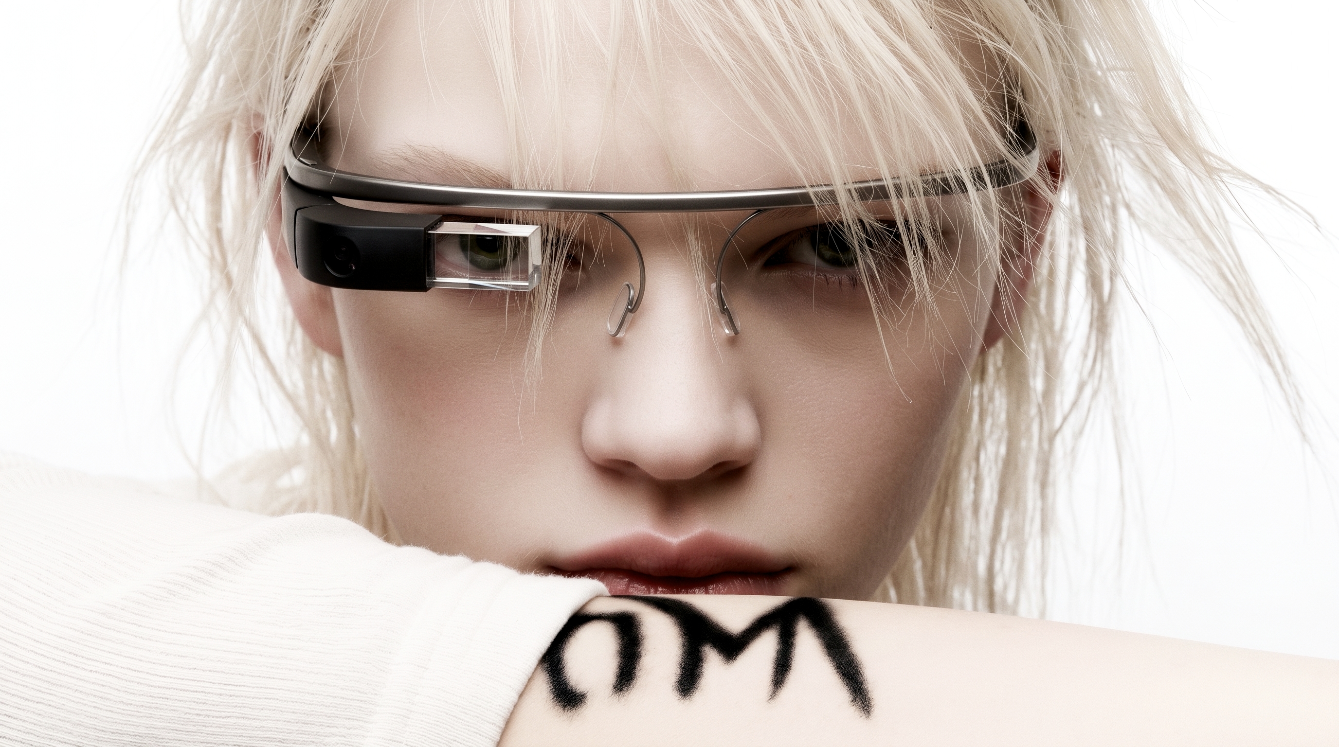 A platinum-haired woman in white knit wears an early head-mounted display with a clear eye prism; OMW is marked on her forearm.