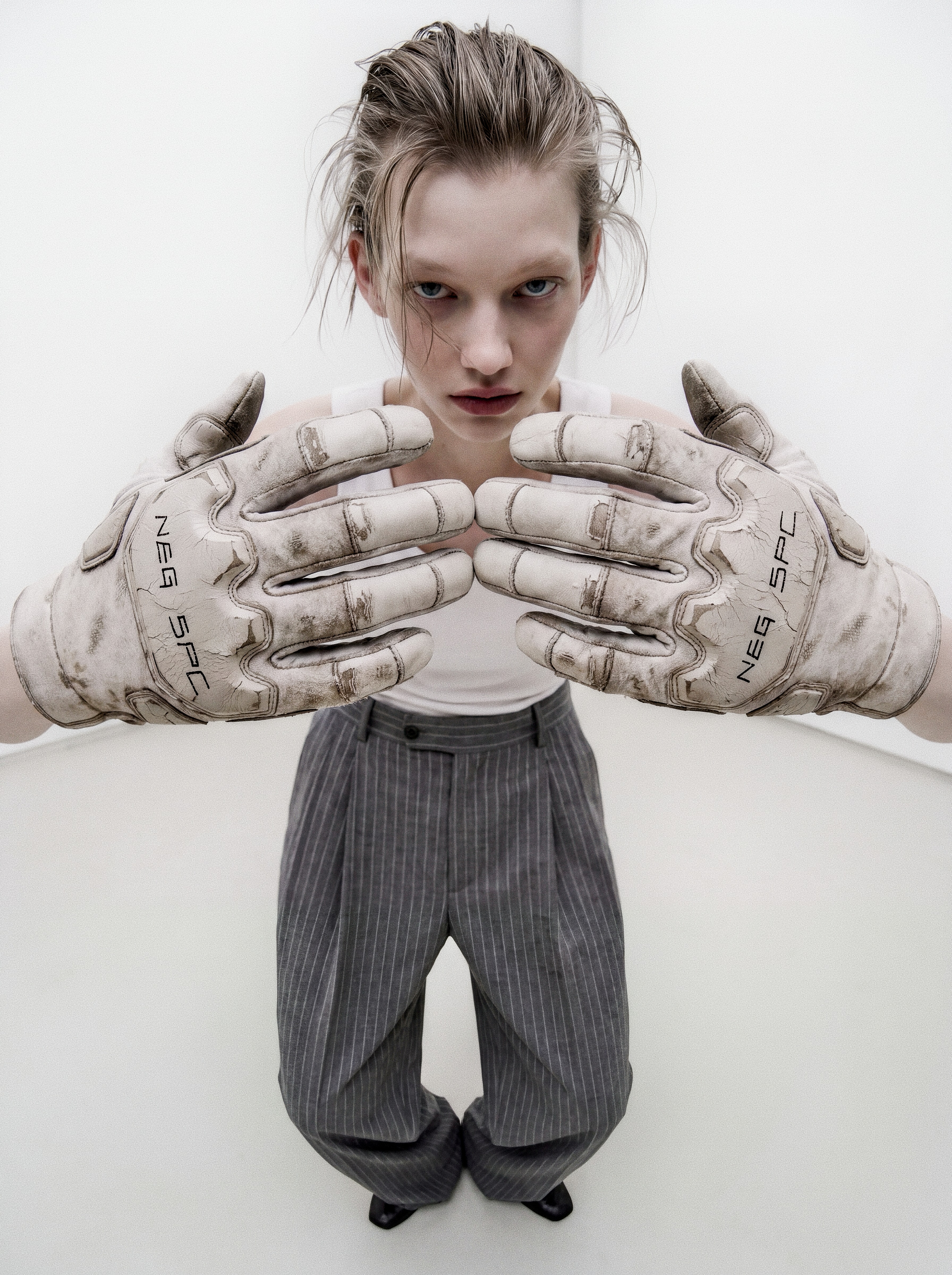 Security still: intern presents both NEG SPC gloves toward the lens in the white room.