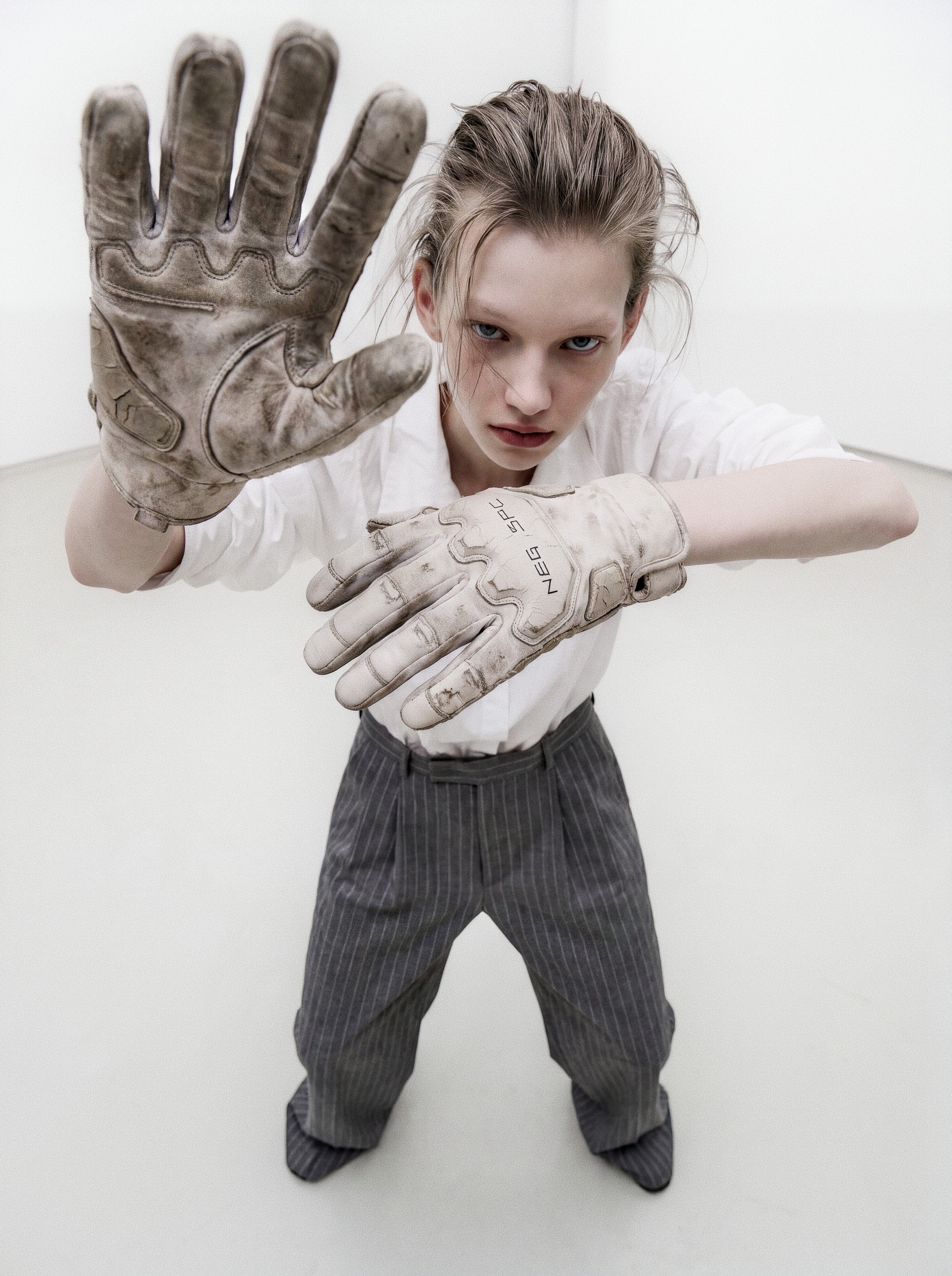 Security still: intern in white gallery thrusts a dirt-stained NEG SPC work glove toward the camera during a live rehang.
