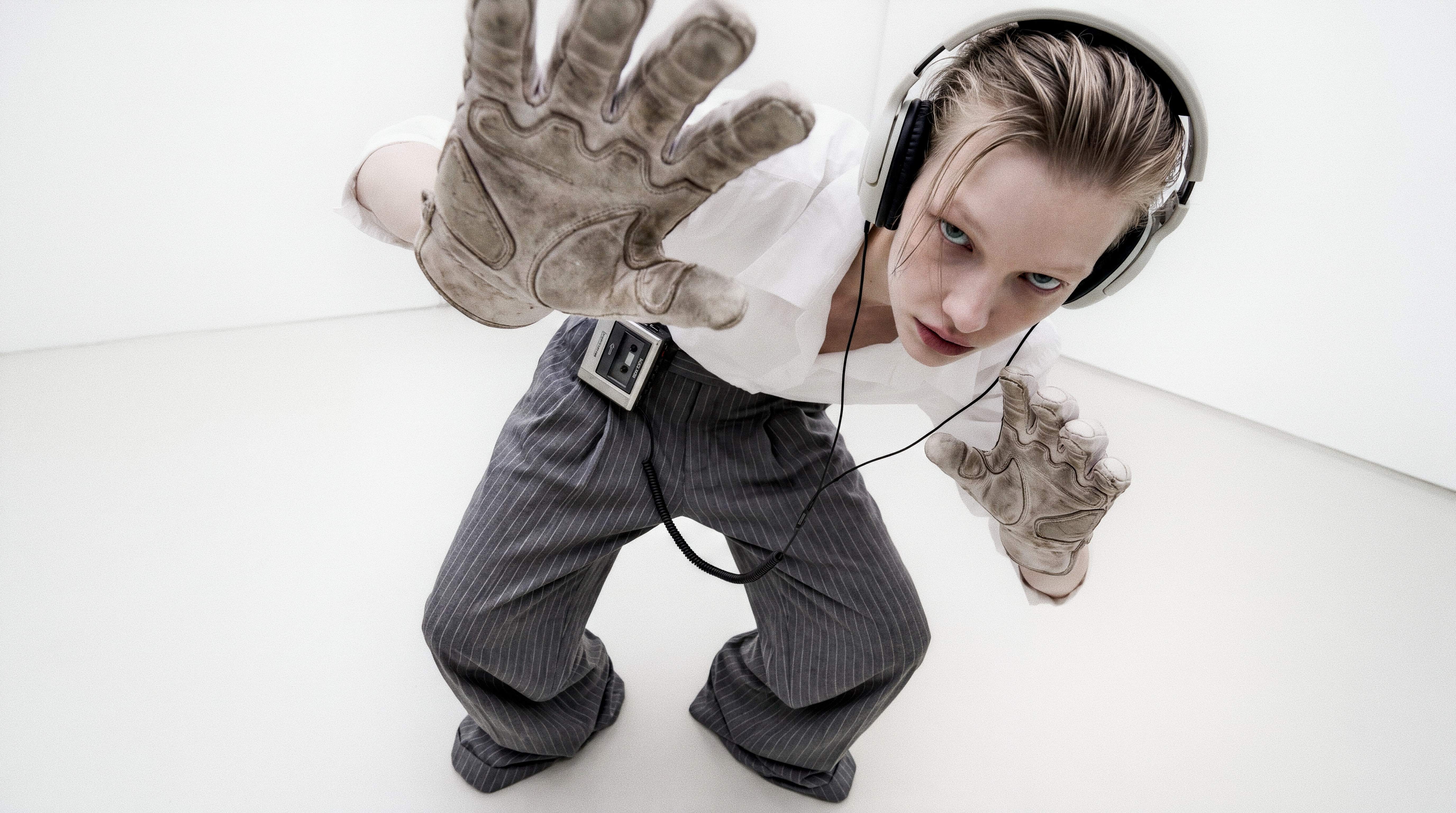 Security still: crouching intern with Walkman and work gloves reaches toward the camera in the open gallery.