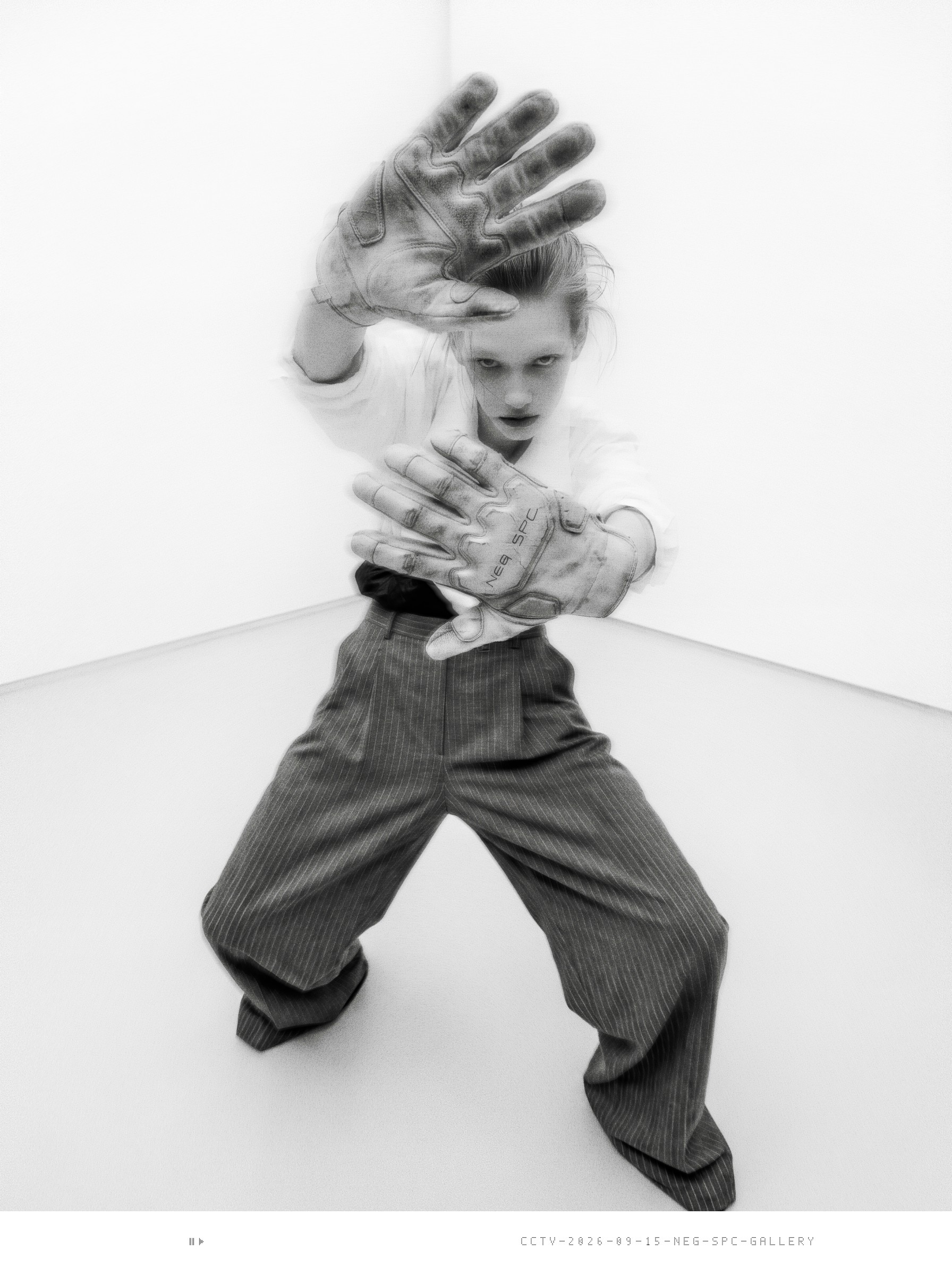 Security still: intern in a white gallery corner holds both dirty work gloves toward the camera.