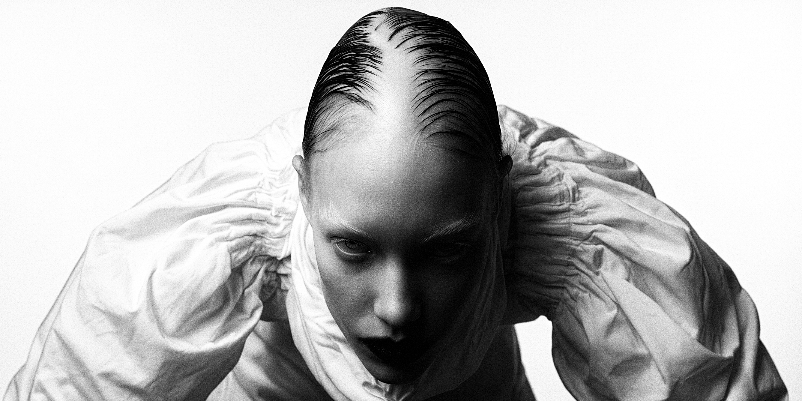 Close-up of a person in a white gathered blouse, wet-look hair, looking into the camera.