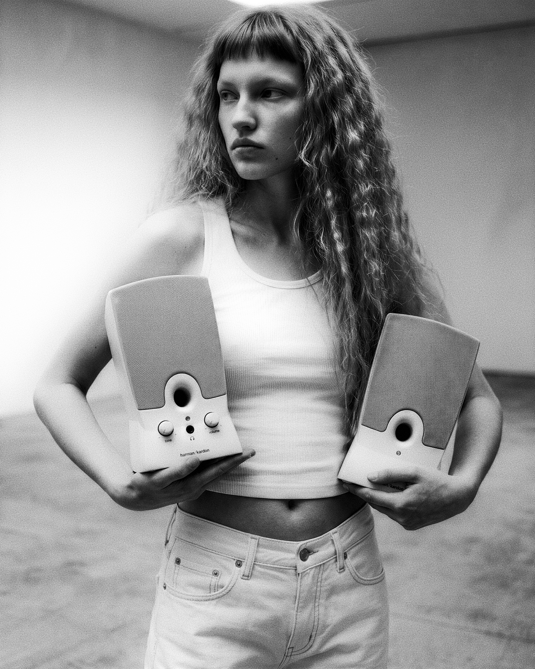 Museum of Tech — person with long curly hair in a white tank and jeans holding two Harman Kardon speakers.