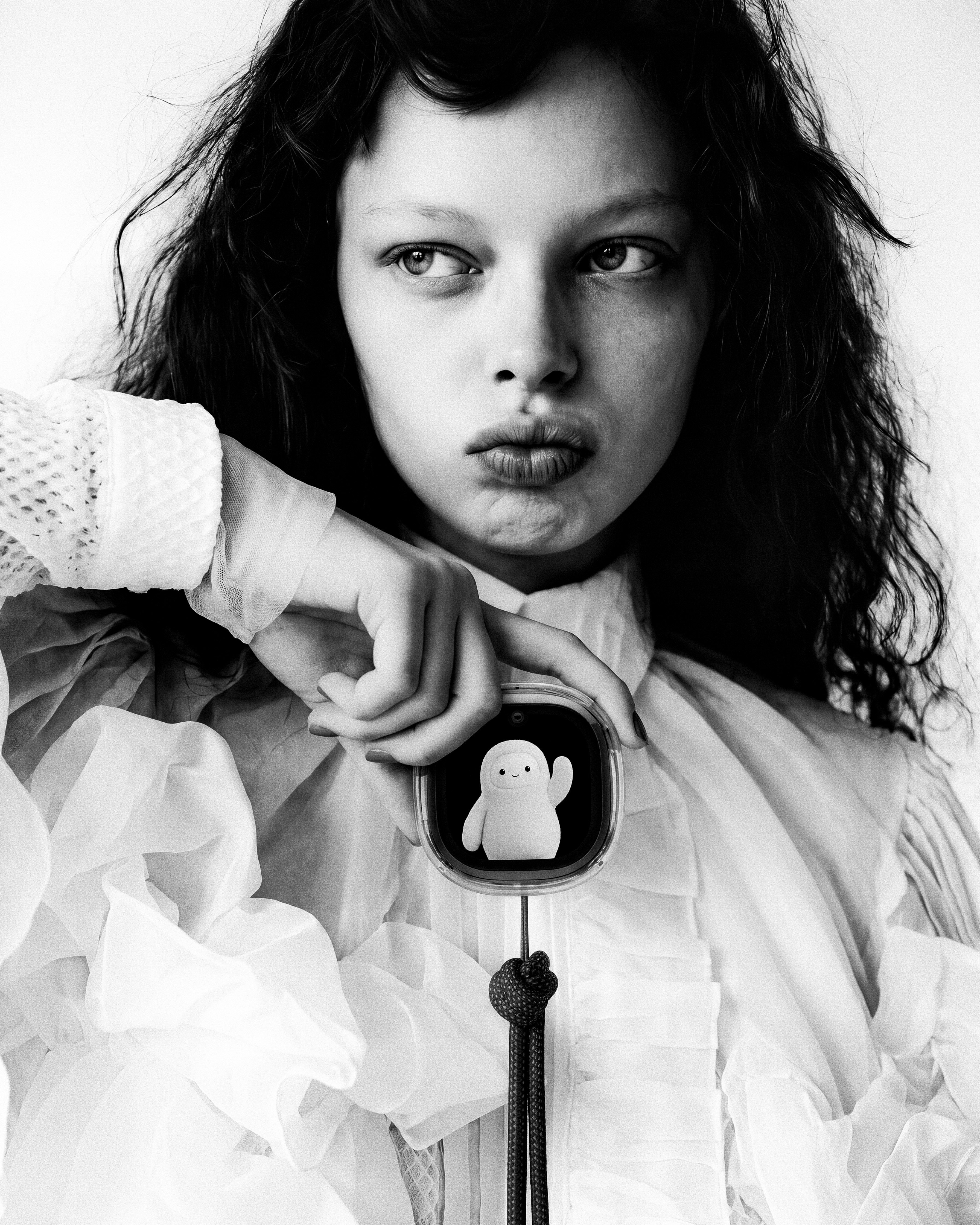 Portrait of model in white bonnet holding the Muse Charm up by her cheek with focused forward gaze.