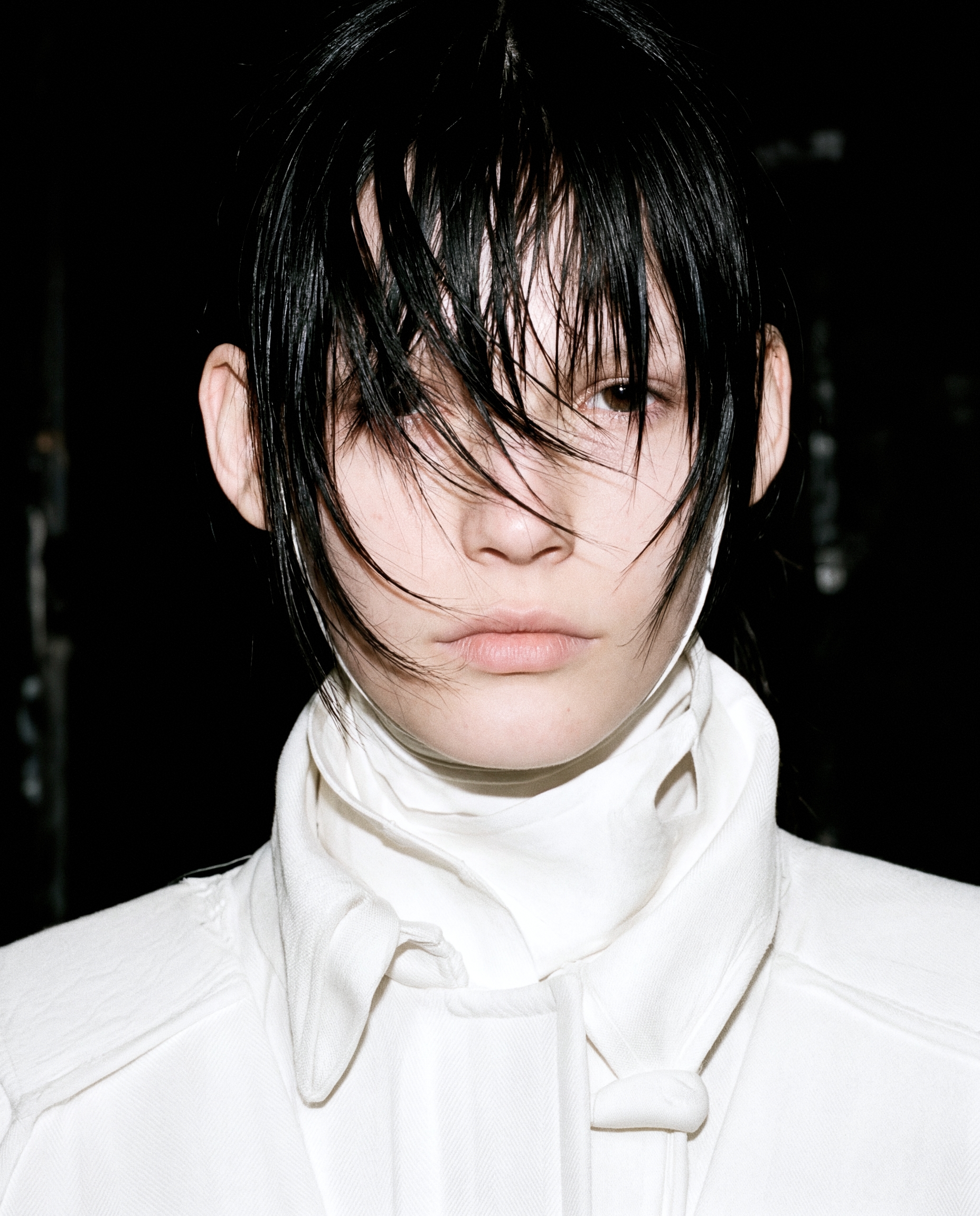 Runway model with dark wet-look fringe in high-neck white collar.