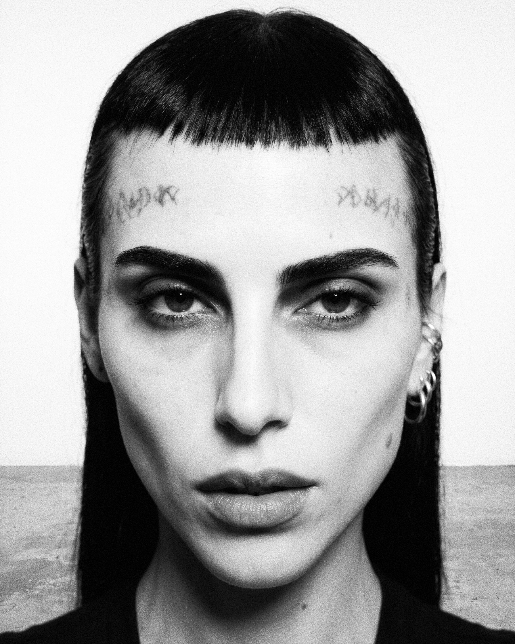 Black-and-white high-contrast beauty portrait with short blunt fringe and eyebrow markings.