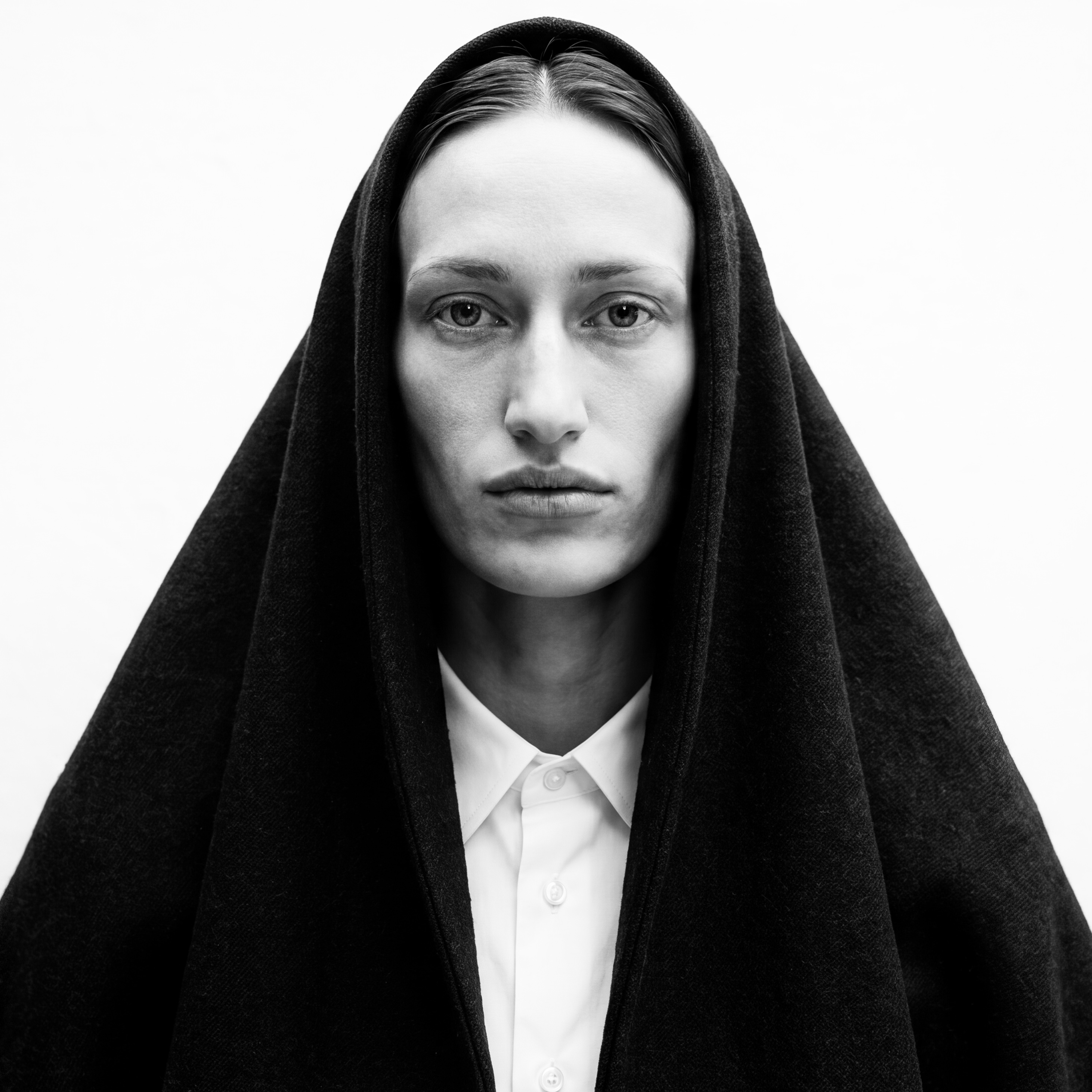 NIIA — monochrome frontal portrait in a black wool cowl over a crisp white collared shirt.