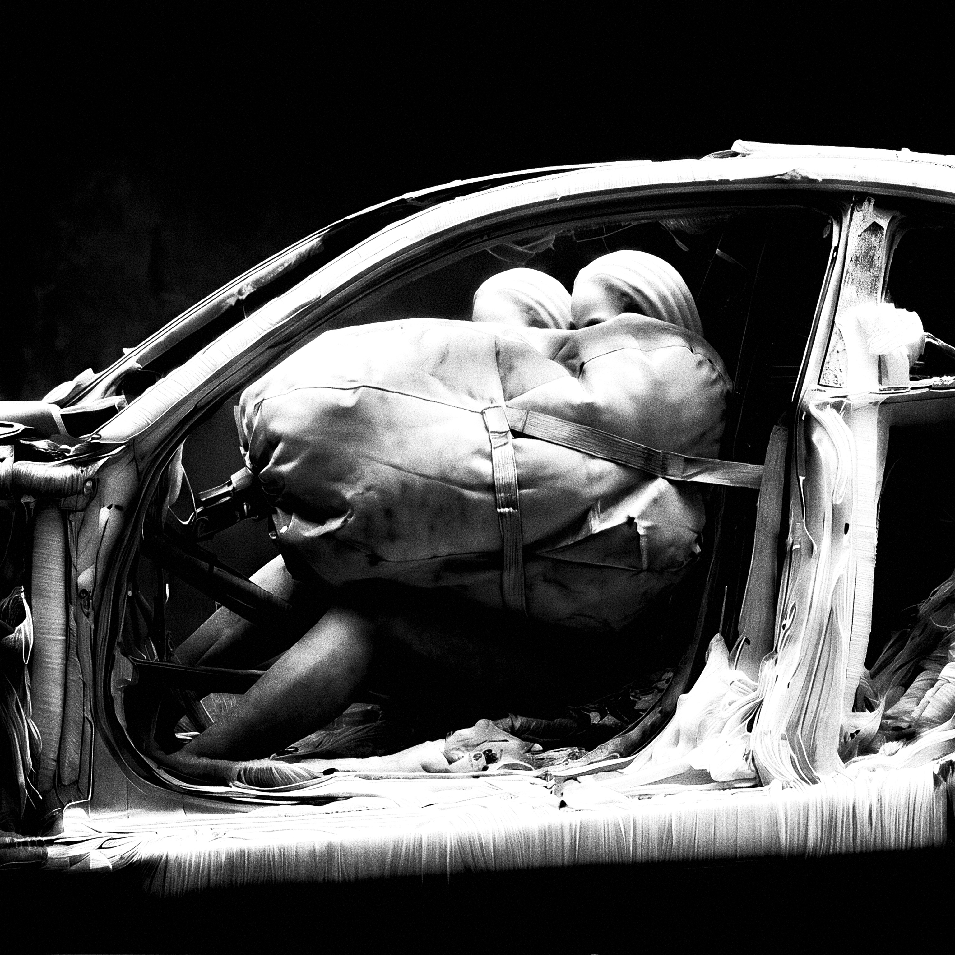 Monochrome cutaway car cabin with two bandaged figures pressed into an inflated airbag held by a seat-belt strap.